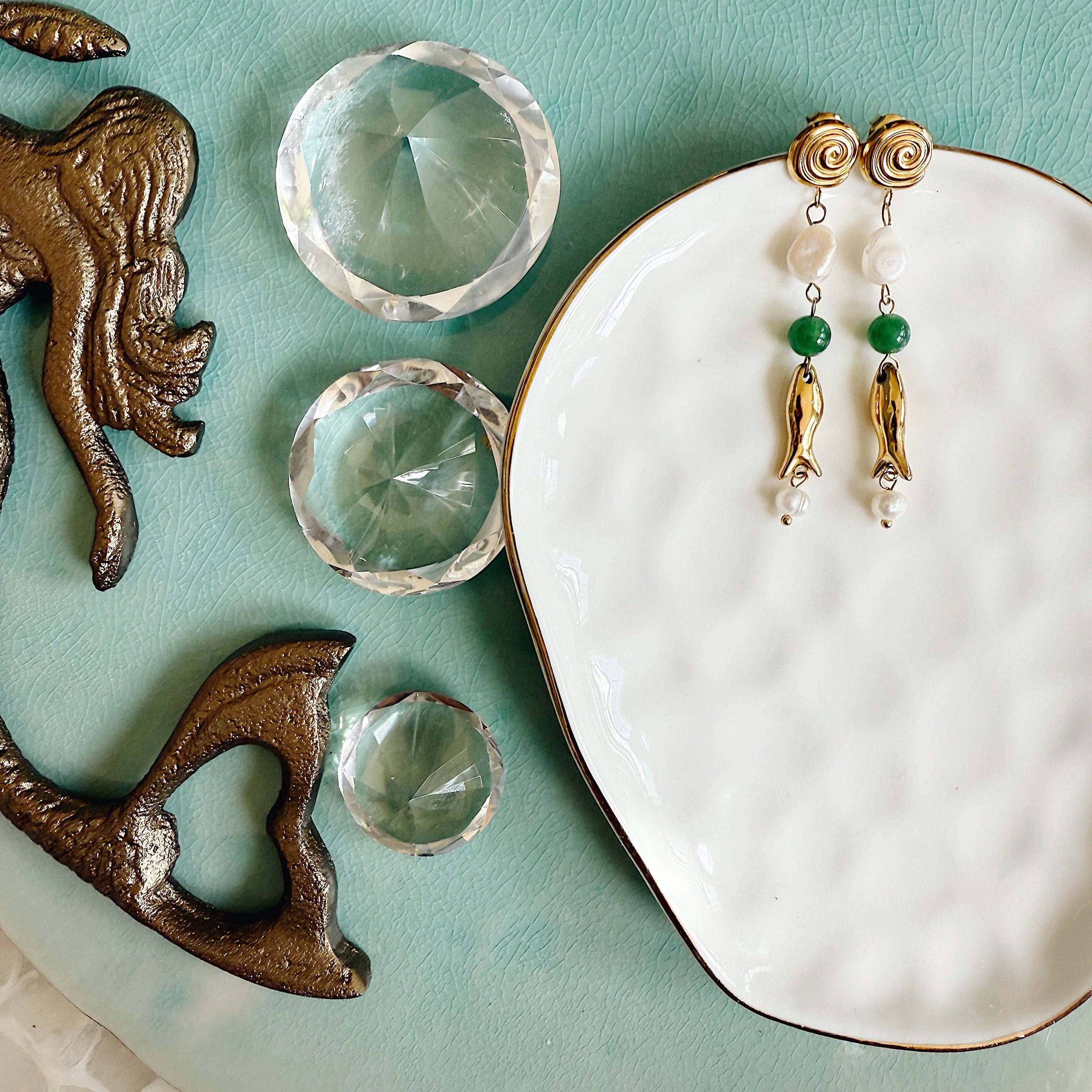 The Nixie Earrings with freshwater pearls and jade stones set in gold, styled against a soft beach-toned background for an airy, feminine look.