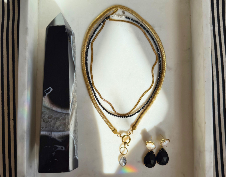 Black and gold jewelry and crystals styled on linen with candlelight — Practical Magic Collection by Wild Alabaster.