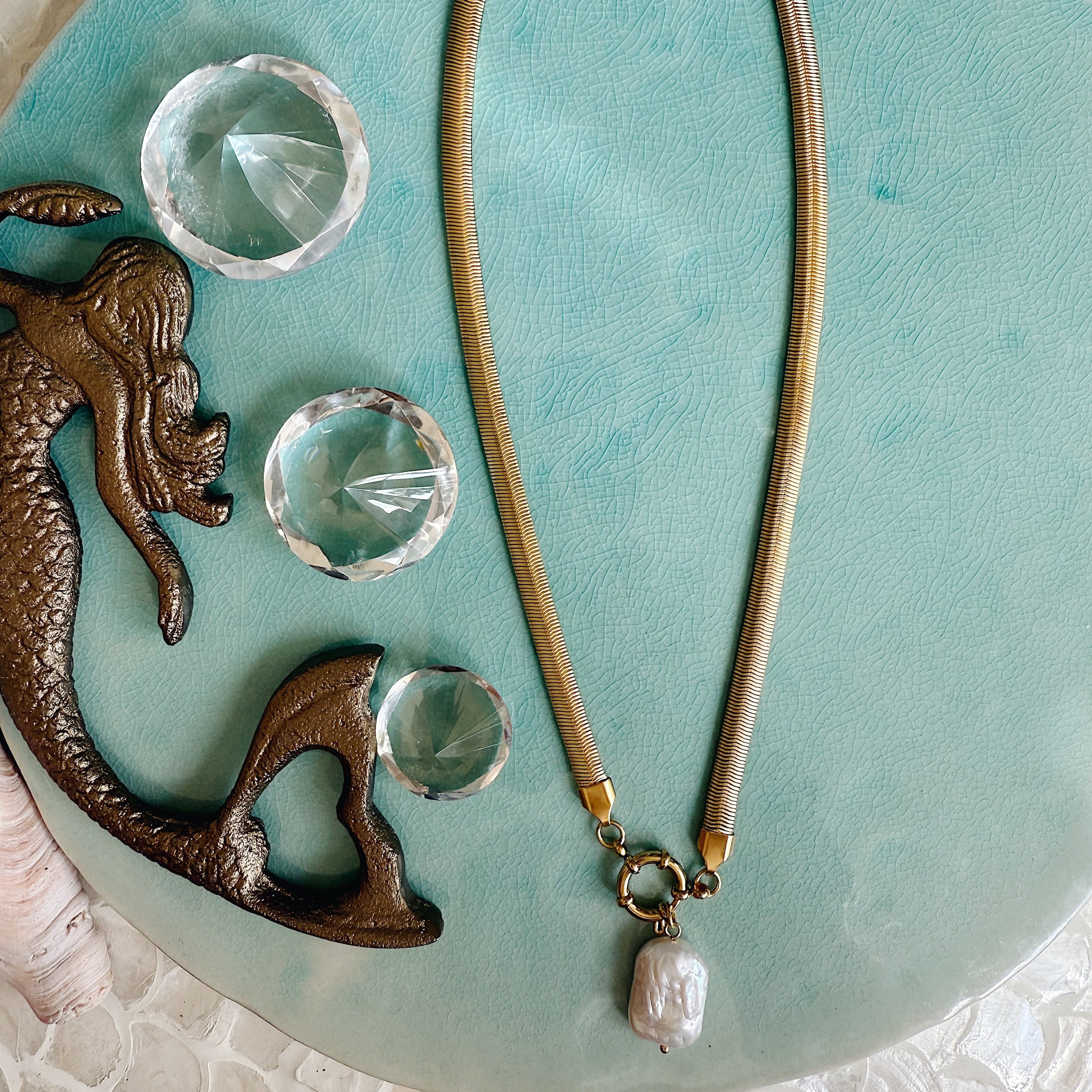 Gold herringbone chain necklace with a single freshwater pearl pendant styled on linen fabric, capturing soft sunlight and coastal-inspired elegance.