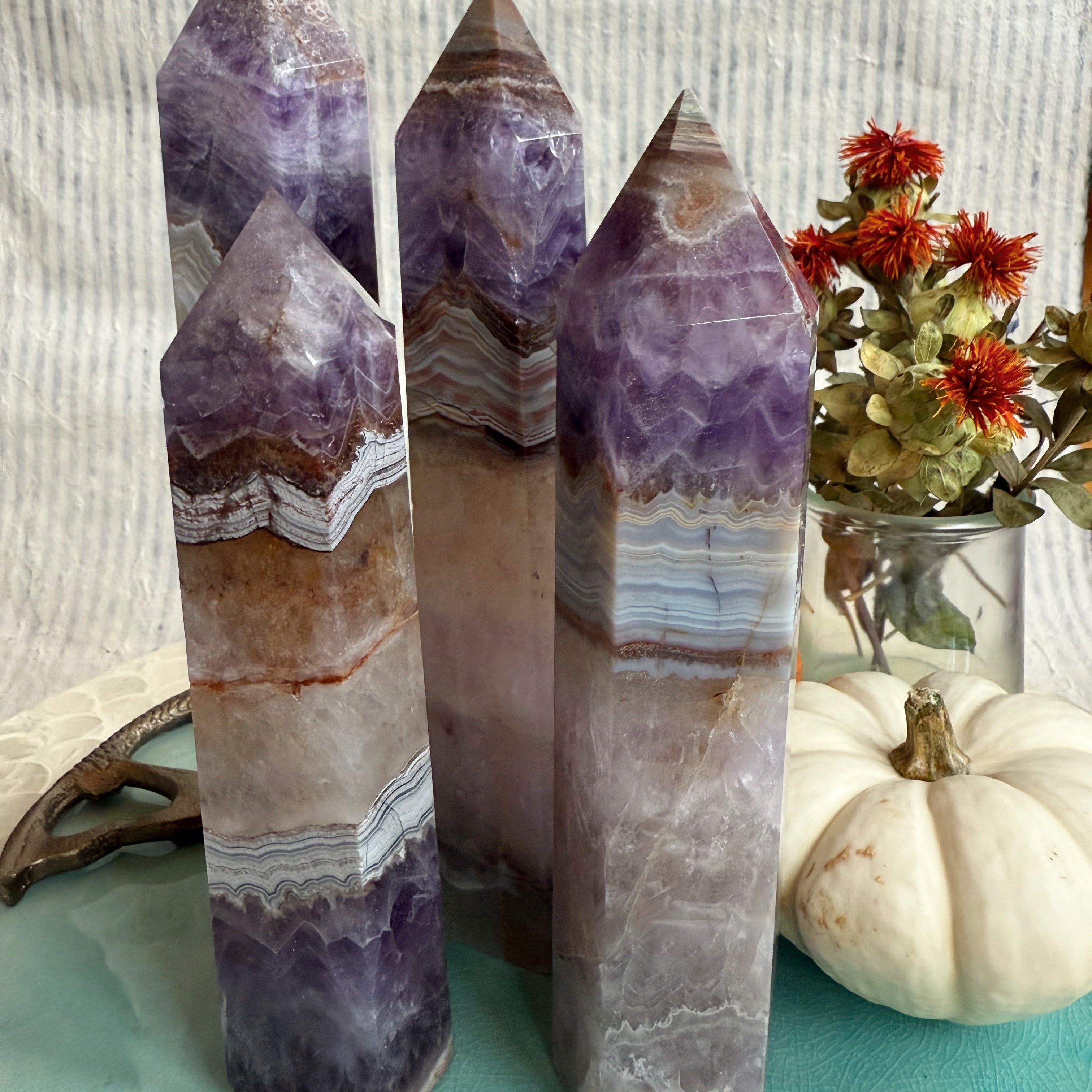 Banded Agate and Amethyst Tower crystals with natural layers of purple and earth tones — symbolizing grounding, clarity, and transformation — from Wild Alabaster’s Autumn Alchemy Collection.