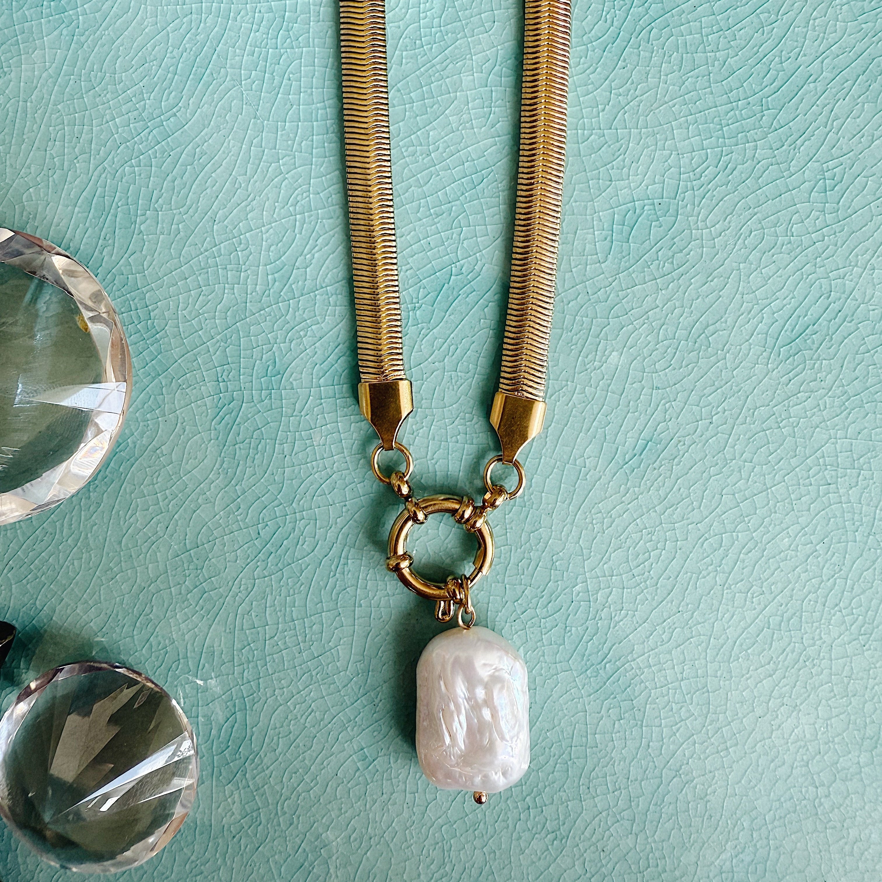 Gold herringbone chain necklace with a single freshwater pearl pendant styled on linen fabric, capturing soft sunlight and coastal-inspired elegance.